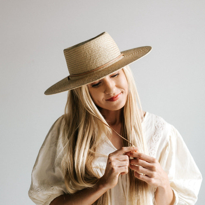 Woman wearing a cream straw hat with a band and a white top against a plain background #color_cream