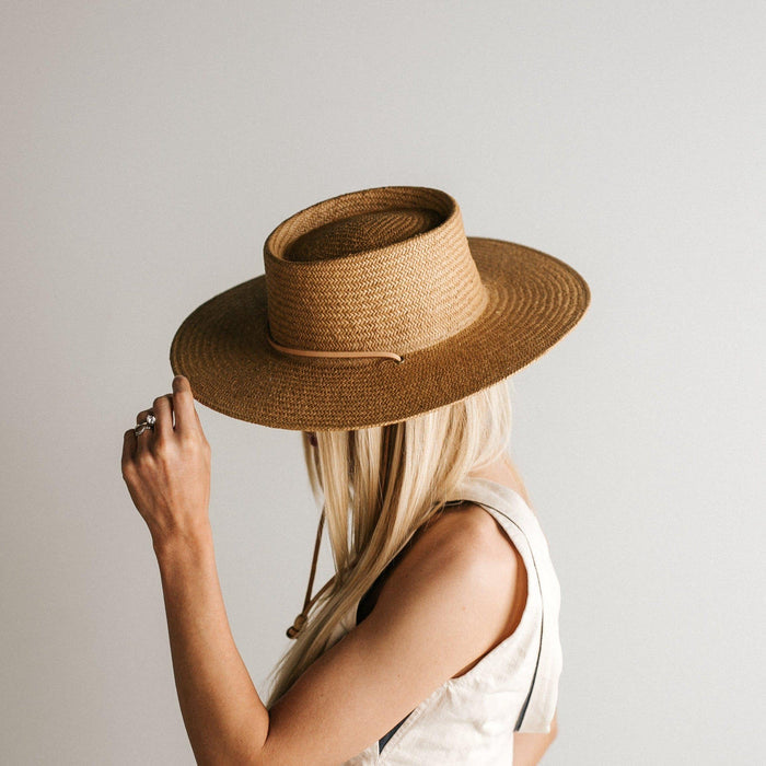 Woman wearing a natural colored straw hat with a band and a white top, facing sideways against a plain background #color_natural
