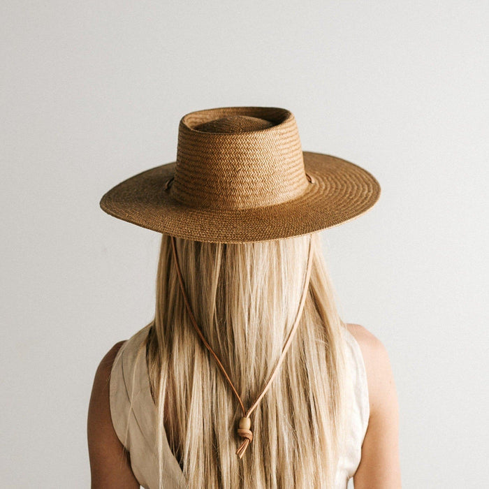 Woman wearing a natural colored straw hat with a band and a white top, facing behind against a plain background #color_natural