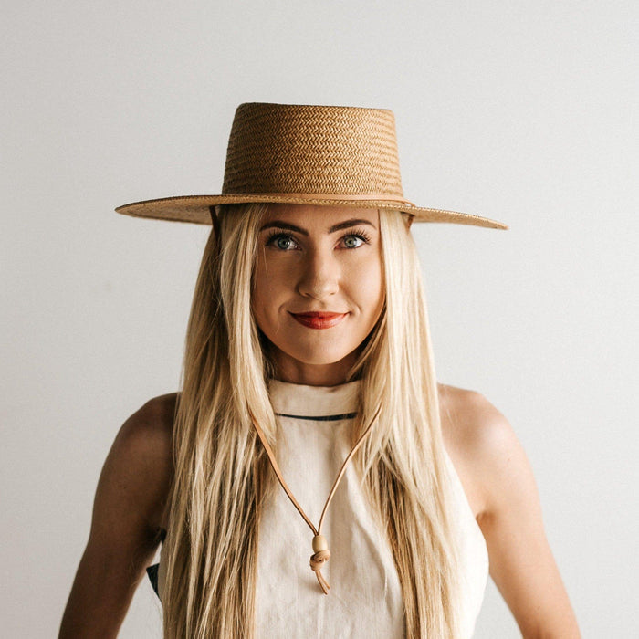 Woman wearing a natural colored straw hat with a band and a white top against a plain background #color_natural