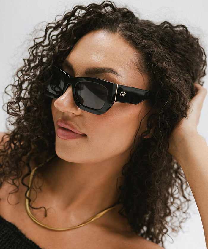Woman wearing black sunglasses and a gold chain against a plain background  #color_black