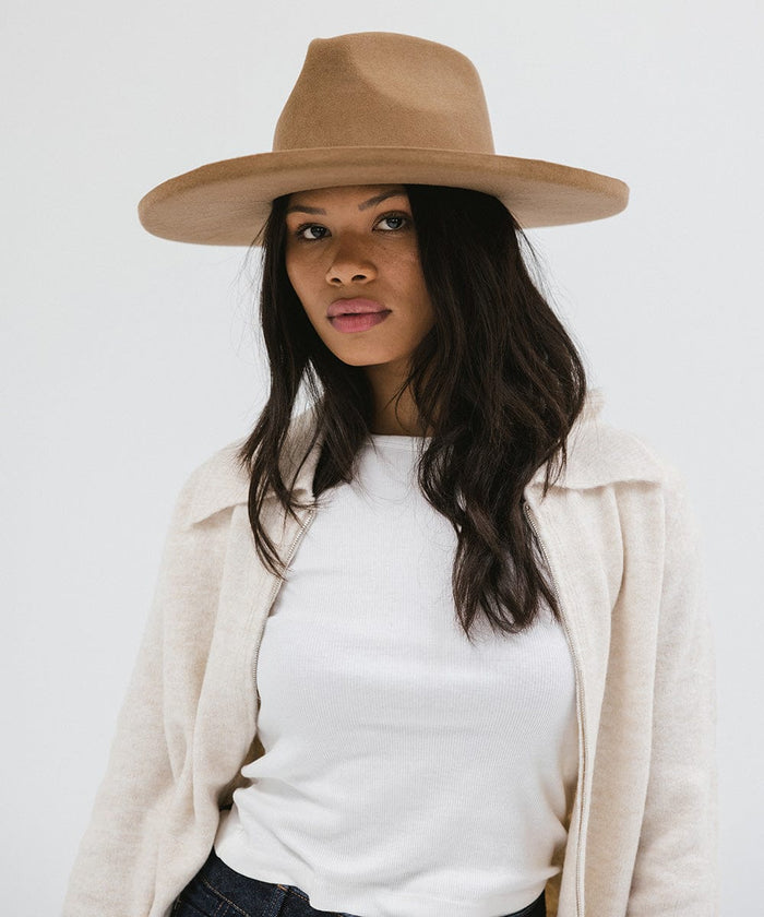 Woman wearing a brown pencil brim fedora hat and a white top with a cream jacket against a white background #color_brown