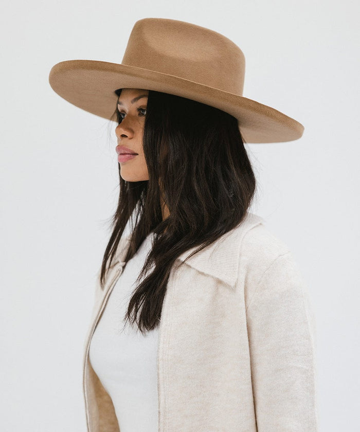 Woman wearing a brown pencil brim fedora hat and a white top with a cream jacket, facing sideways against a white background #color_brown