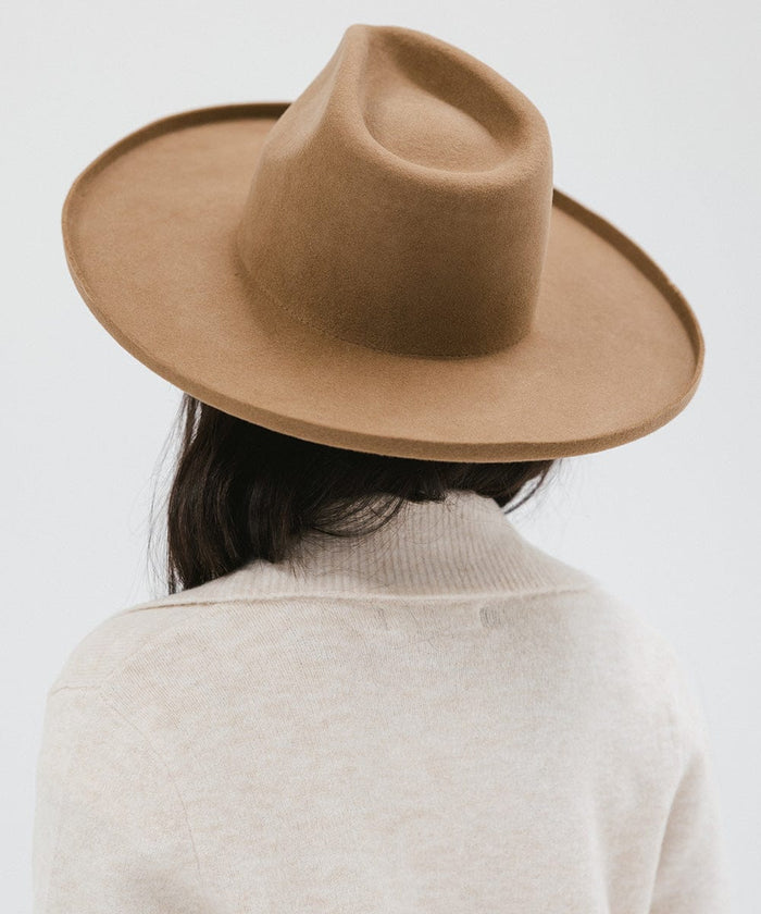 Woman wearing a brown pencil brim fedora hat and a cream jacket, facing behind against a white background #color_brown