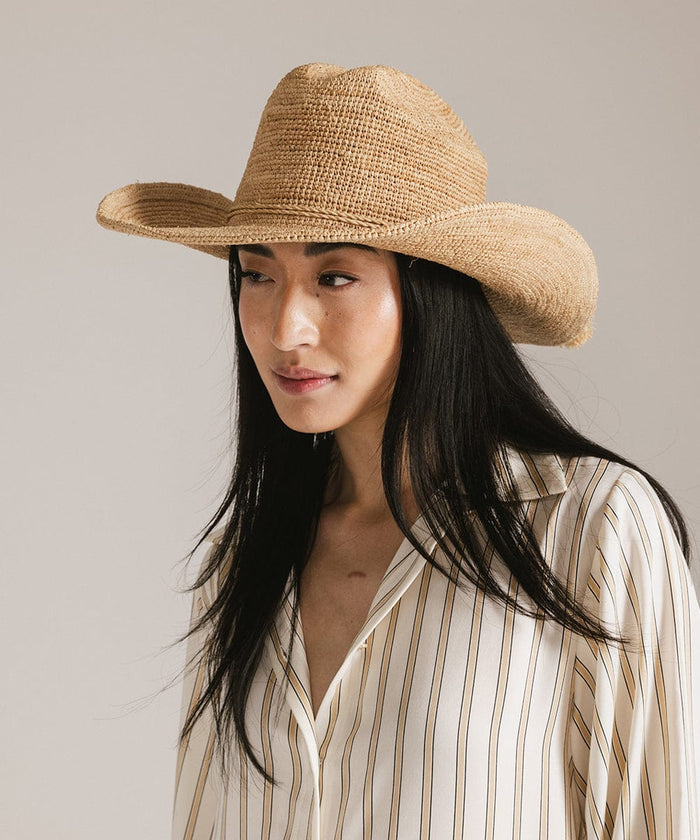 Woman wearing a natural colored straw cowboy hat and a light colored shirt, looking sideways against a plain background #color_natural