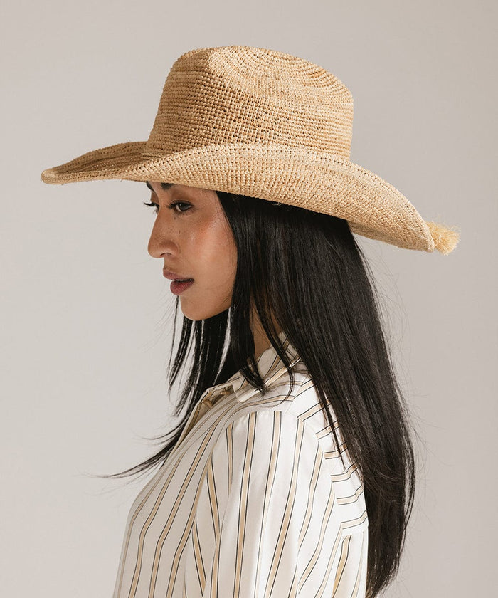 Woman wearing a natural colored straw cowboy hat and a light colored shirt, facing sideways against a plain background #color_natural