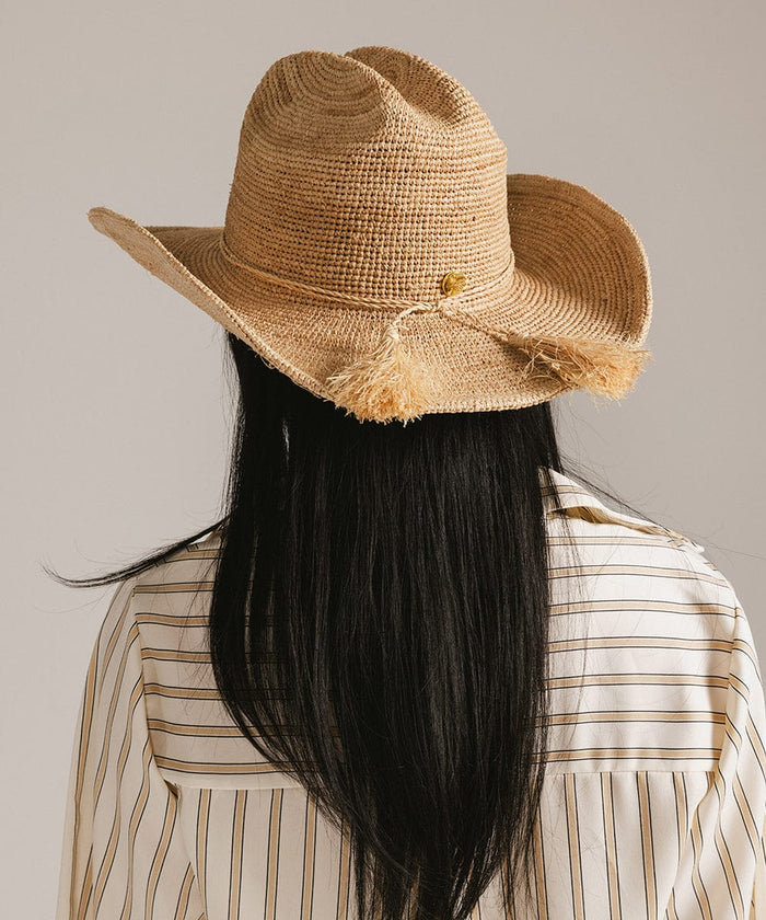 Woman wearing a natural colored straw cowboy hat with a band and a light colored shirt, facing behind against a plain background #color_natural
