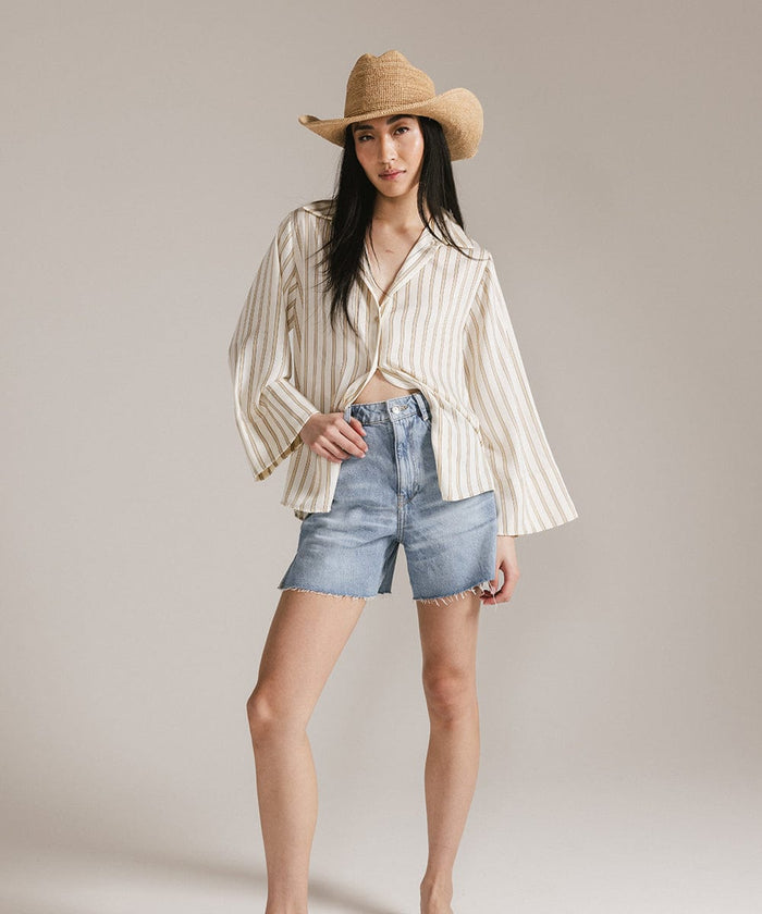 Woman wearing a natural colored straw cowboy hat, a light colored shirt and denim shorts against a plain background #color_natural