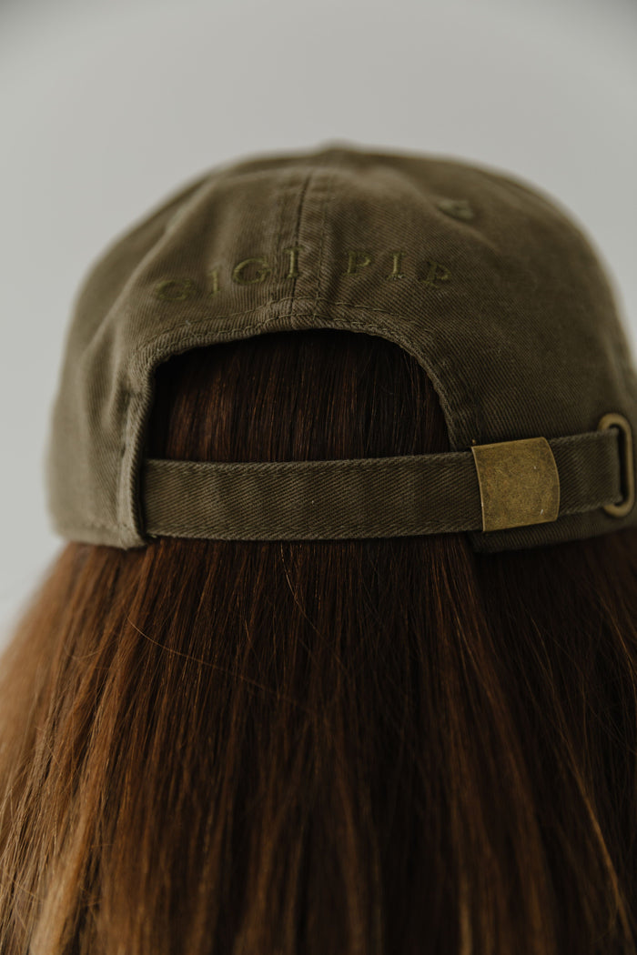 Woman wearing an olive colored ball cap facing behind against a plain background #color_olive