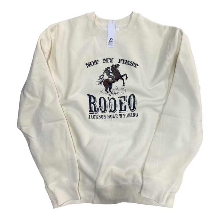 A bone-colored sweatshirt with the text 'NOT MY FIRST RODEO JACKSON HOLE WYOMING' printed on the front.