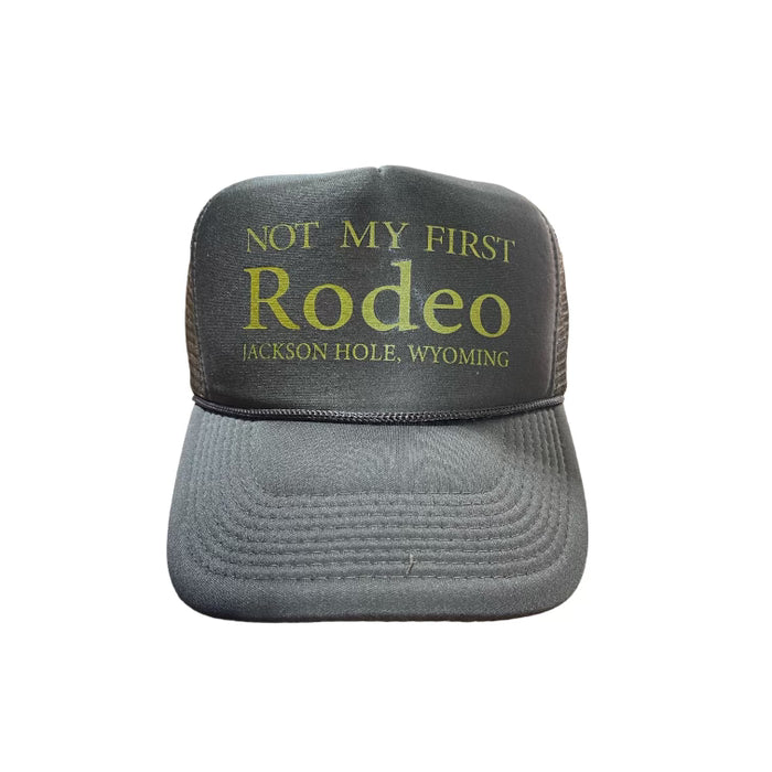 A brown trucker cap with the text 'NOT MY FIRST Rodeo JACKSON HOLE, WYOMING' printed on the front.