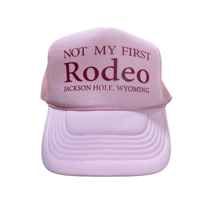 A pink trucker cap with the text 'NOT MY FIRST Rodeo JACKSON HOLE, WYOMING' printed on the front.