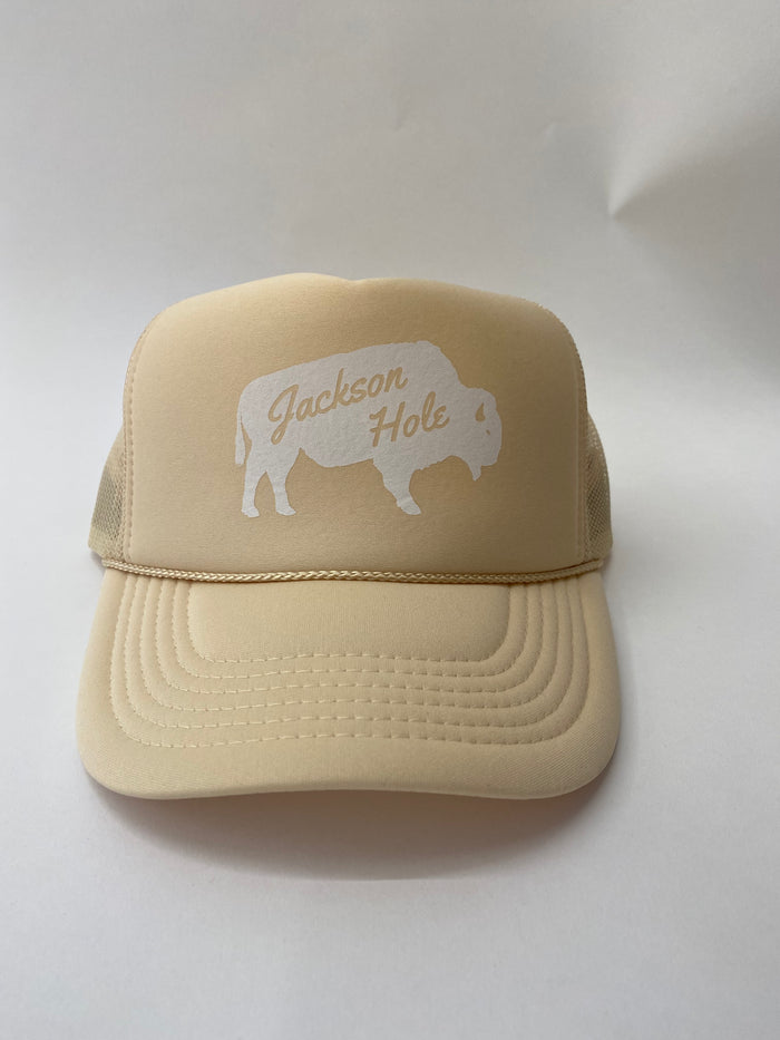 A cream trucker hat with 'Jackson Hole' text and a silhouette of a bison on the front.