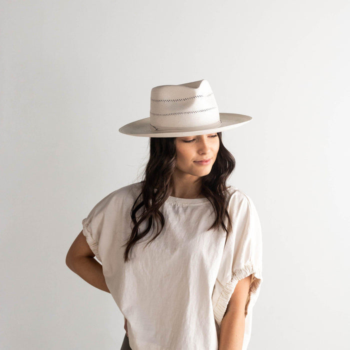 Woman wearing a cream fedora straw hat with a hat band and a white t-shirt against a plain background #color_cream