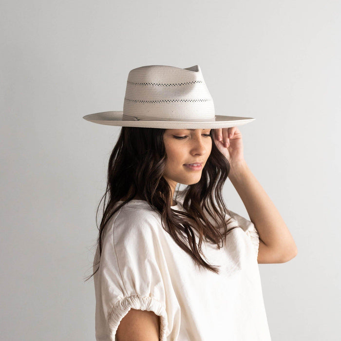 Woman wearing a cream fedora straw hat with a hat band and a white t-shirt, facing sideways against a plain background #color_cream