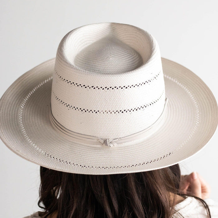 Person wearing a cream fedora straw hat with a hat band against a plain background #color_cream