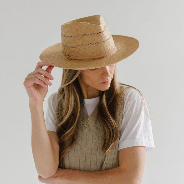 Woman wearing a honey colored straw fedora hat with a hat band and a white t-shirt with a beige sleeveless sweater, posing against a plain background #color_honey