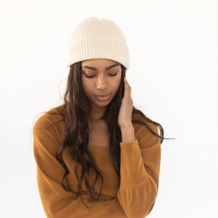 Woman wearing an oatmeal colored knit beanie and a brown sweatshirt against a plain background #color_oatmeal