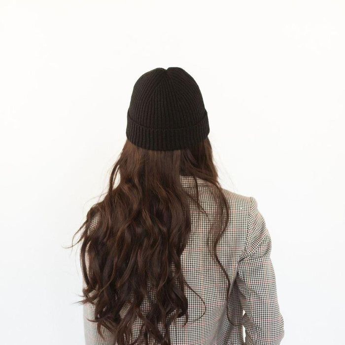 Woman wearing a black colored knit beanie and a blazer, facing behind against a plain background #color_black