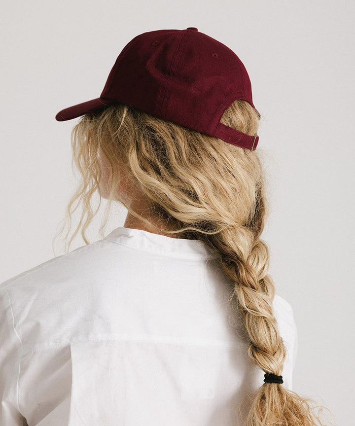 Woman wearing a burgundy cap and a white shirt, facing behind against a plain background  #color_burgundy