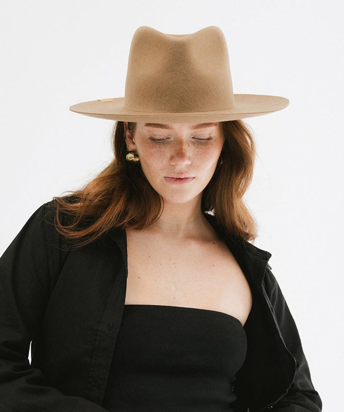 Woman wearing a brown fedora hat and a lack top with a black shirt against a plain background #color_brown