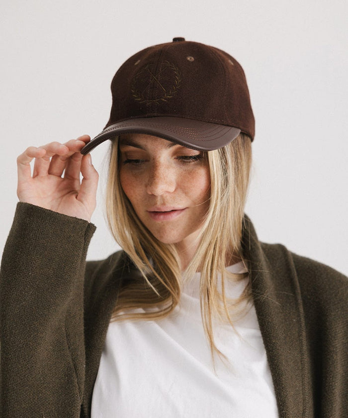 Woman wearing a brown cap with a logo and a white t-shirt with a brown coat, posing against a plain background  #color_brown