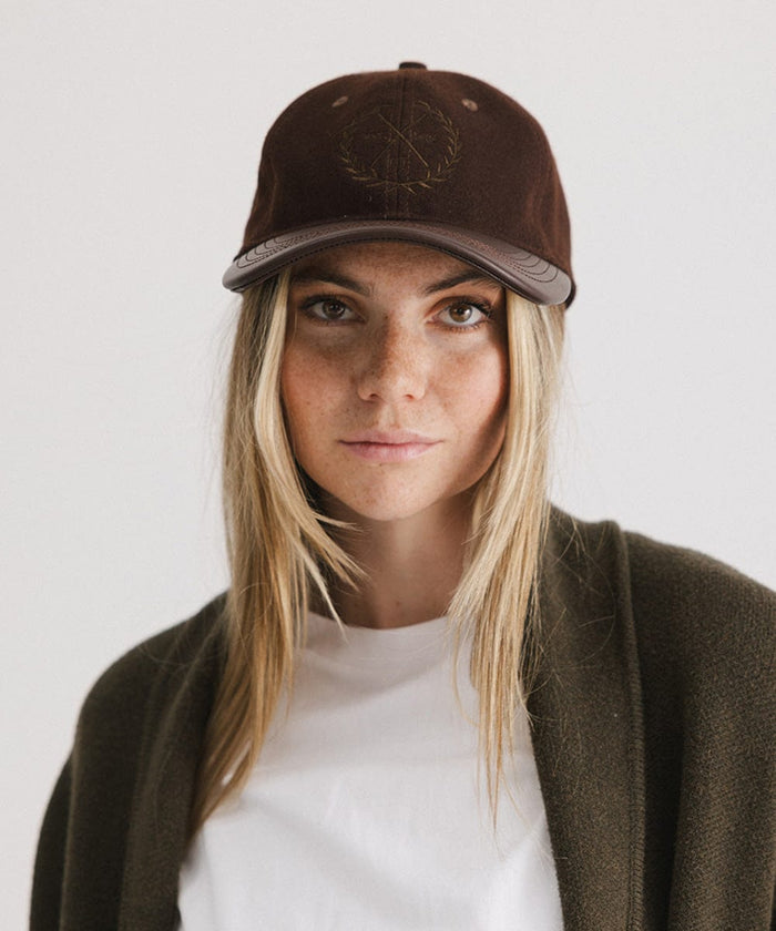 Woman wearing a brown cap with a logo and a white t-shirt with a brown coat against a plain background  #color_brown