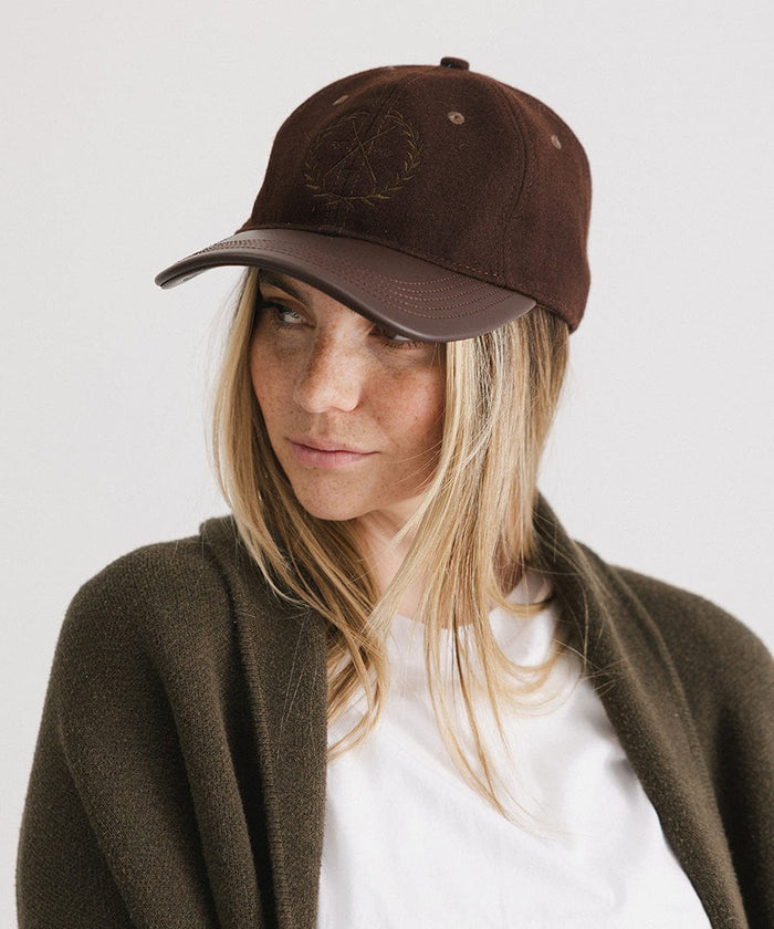 Woman wearing a brown cap with a logo and a white t-shirt with a brown coat, looking sideways against a plain background  #color_brown