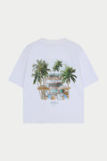 White t-shirt with a tropical design featuring palm trees and a beach club on a white background