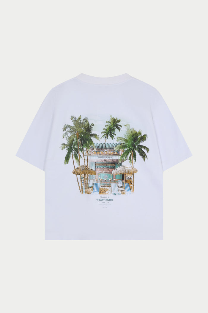 White t-shirt with a tropical design featuring palm trees and a beach club on a white background
