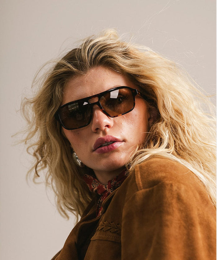 Person wearing sunglasses and a brown jacket with a neutral background #color_tortoise