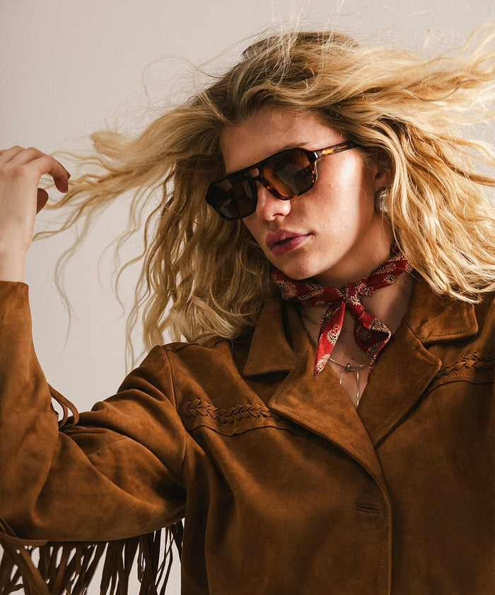 Woman wearing sunglasses and a brown coat with a red scarf, against a neutral background #color_tortoise