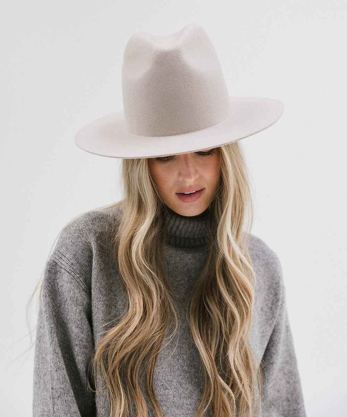 Woman wearing an ivory colored hat and grey sweater, looking down against a white background #color_ivory