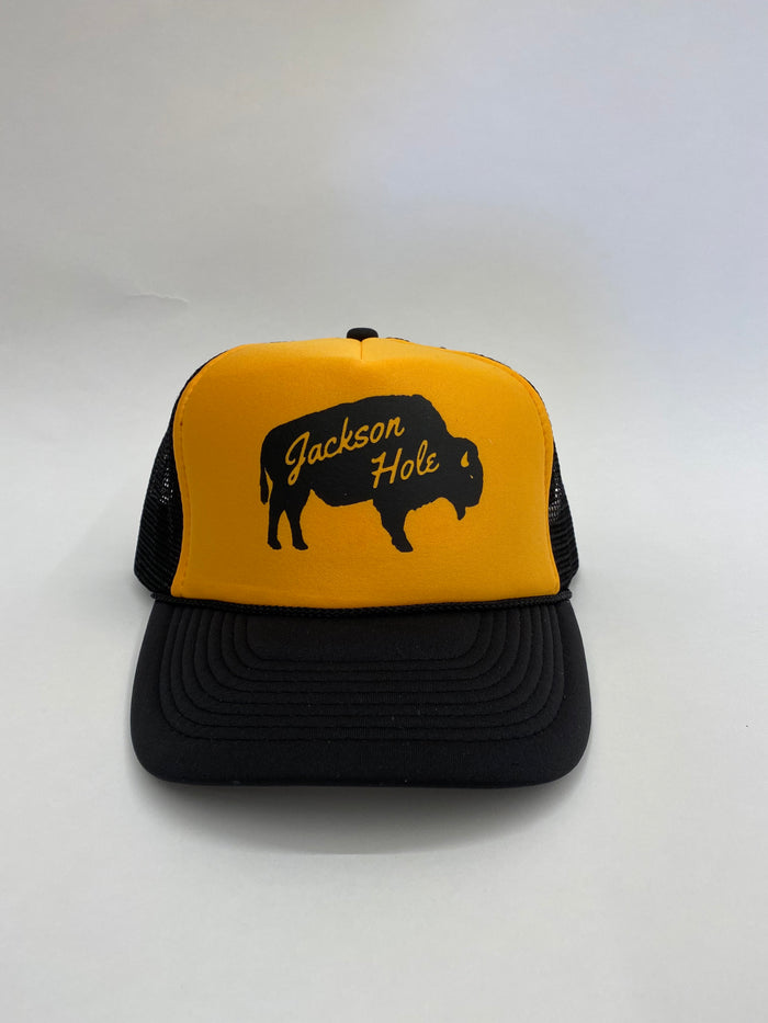 A gold and black trucker hat with 'Jackson Hole' text and a silhouette of a bison on the front.