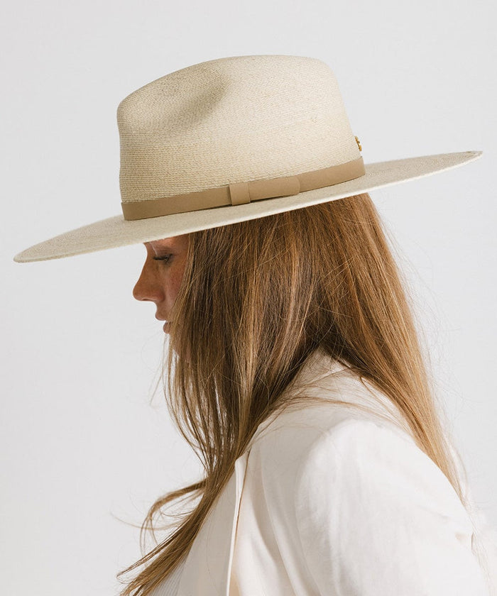 Woman wearing a natural colored wide brim fedora hat with a hat band and a cream blazer, facing sideways against a plain background #color_natural