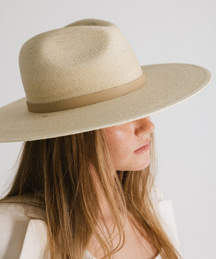 Woman wearing a natural colored wide brim fedora hat with a hat band, looking sideways against a plain background #color_natural