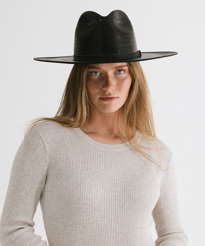 Woman wearing a black wide brim fedora hat with a hat band and a grey t-shirt against a plain background #color_limited edition black