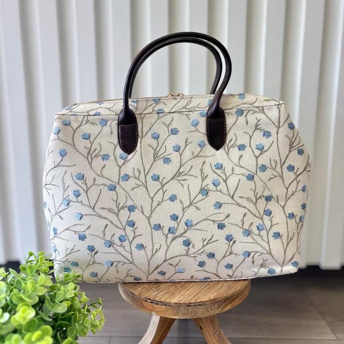 Beige zipper top bag with blue embroidered blossoms.