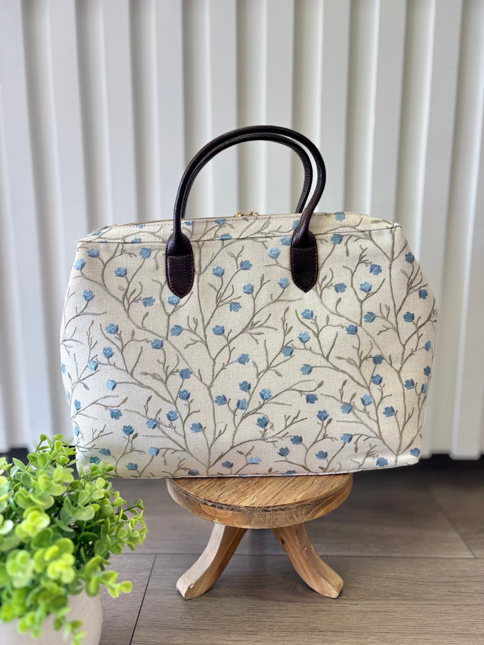 Beige zipper top bag with blue embroidered blossoms.