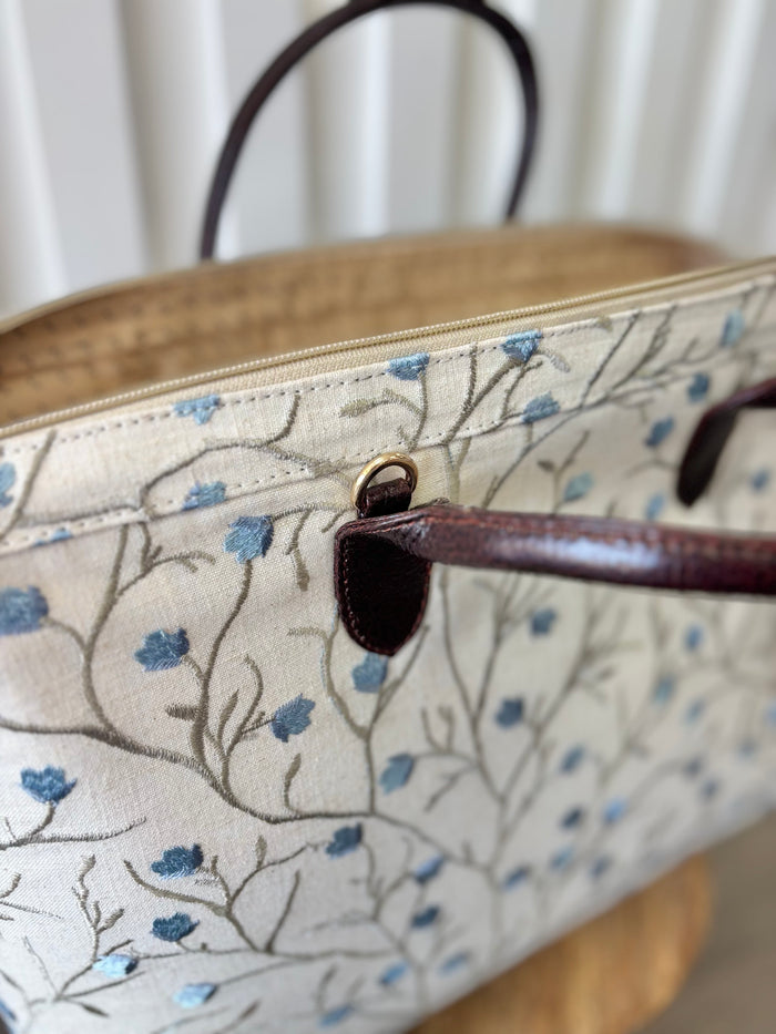 Beige zipper top bag with blue embroidered blossoms.