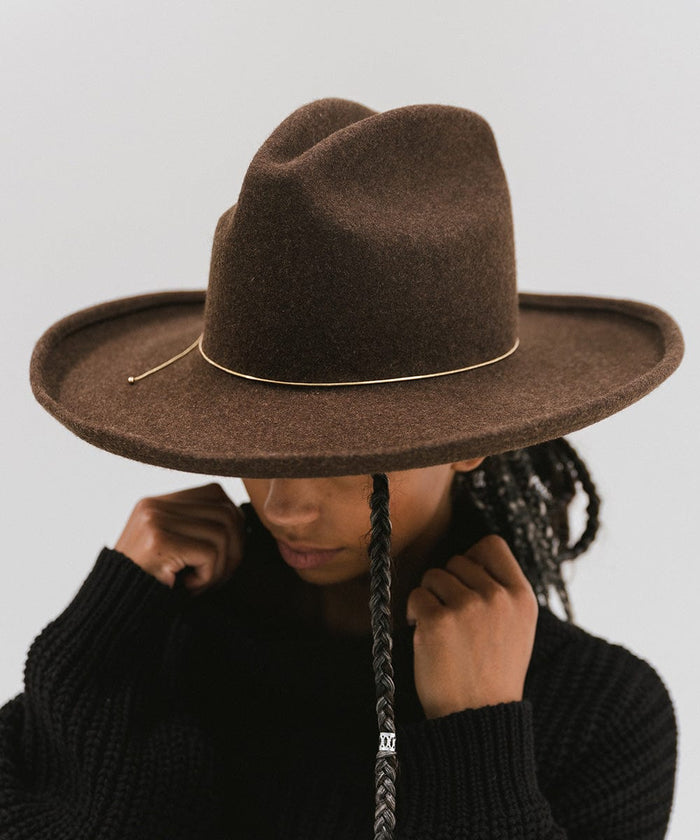 Woman wearing a brown hat with a gold chain bolo hat band and a black sweater, posing against a plain background  #color_gold