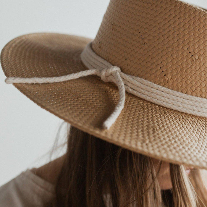 Woman wearing a natural colored straw hat with a white rope hat band against a plain background #color_natural