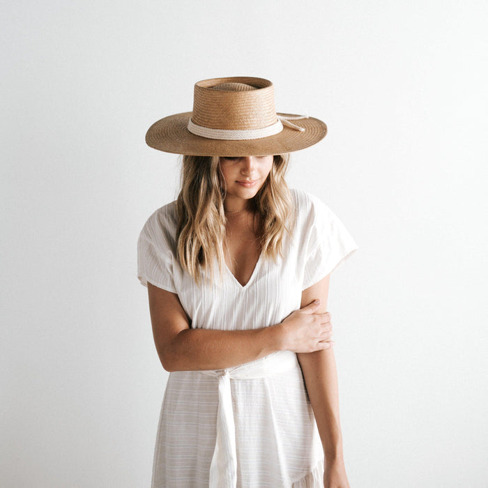 Woman wearing a natural colored straw hat with a white rope hat band and a white dress against a plain background #color_natural