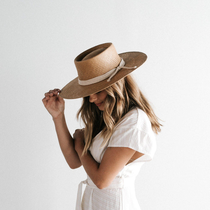 Woman wearing a natural colored straw hat with a white rope hat band and a white dress, looking sideways against a plain background #color_natural