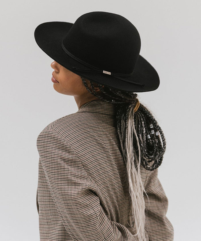 Woman wearing a black fedora hat with a hat band and a checkered coat, facing sideways against a plain background #color_black