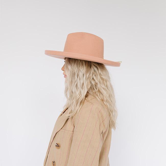 Woman wearing a dusty pink pencil brim fedora hat and a beige blazer, facing sideways against a plain background  #color_dusty pink