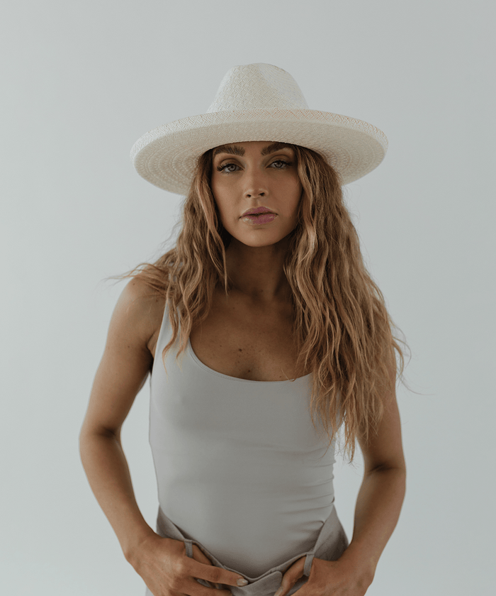 Woman wearing a white pencil brim straw hat and a white top against a plain background #color_white