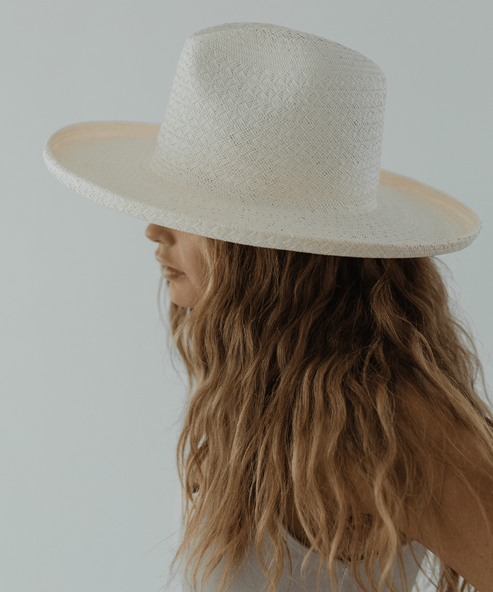 Woman wearing a white pencil brim straw hat and a white top, facing sideways against a plain background #color_white