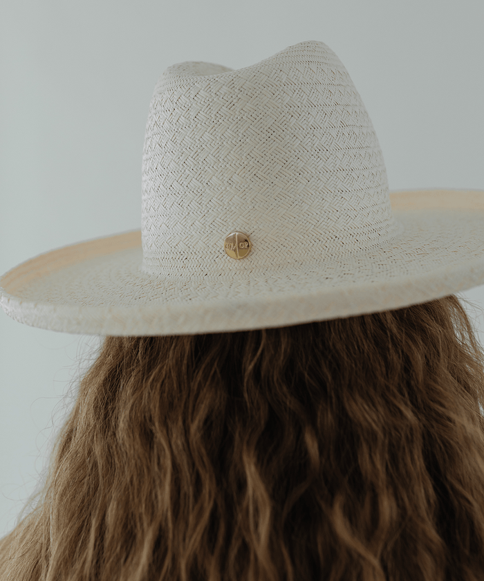 Woman wearing a white pencil brim straw hat against a plain background #color_white