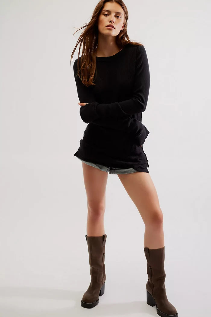 A woman wearing a black crew neck sweater with contrast sleeves and raw hems, paired with denim shorts and boots.